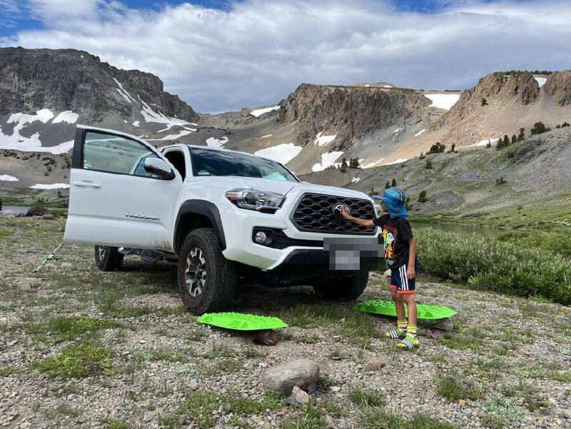 White Toyota Tacoma stopped on a mountain trail with rocky high country terrain and snow patches in the background